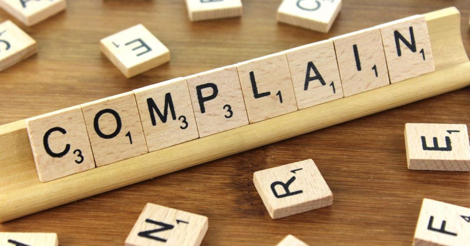 The image contains the word “complain” made on wooden tiles.
